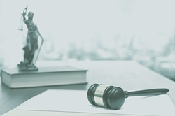 [ai] A wooden gavel lies on a stack of legal documents, with a statue of Lady Justice in the background, symbolizing law and justice in a professional legal setting.